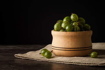 Juicy ripe berries of a gooseberry in a small wooden pot on black surface. Gooseberry harvest