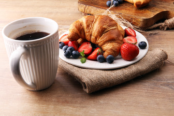 Delicious breakfast with fresh croissants, coffee and ripe berries on old wooden background