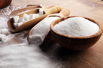 Bowl and scoop with white sand and lump sugar on brown wooden background