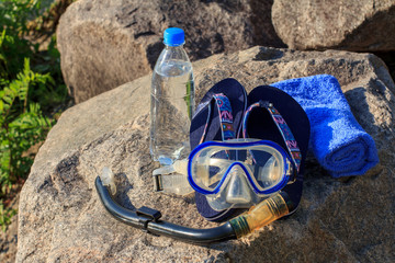 Bottle with water, towel,  flip-flops, mask for diving and snorkel tube lie on stones