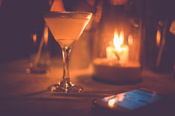 Margarita iced cocktail in martini glasses in front of the night bokeh lights on blurred candle background and mobile phone lying on the table