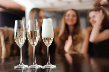 Man fills glasses of champagne for three beautiful young women in restaurant