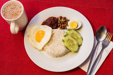 Malaysian Food - Nasi Lemak and Frothy Teh Tarik on a red background. Both dishes are unofficially the national breakfast dish of Malaysia. Teh tarik is basically a Tea with Milk