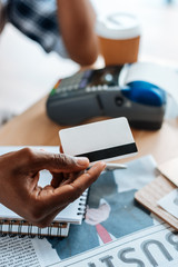 cropped view of african american man working with credit card and terminal in coffee shop