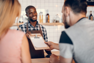 handsome cheerful african american barista giving menu to clients on bar counter in cafe