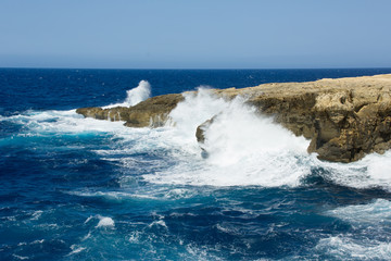 Wild waves of blue sea spatter on rocky shore of Gozo, Malta