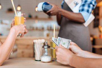 cropped view of people paying with cash, waiter standing behind in cafe