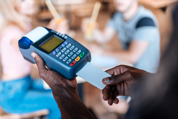 cropped view of african american waiter with terminal taking payment with credit card in cafe