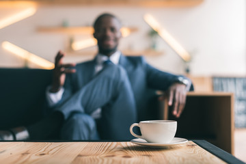 Fototapeta na wymiar selective focus of african american businessman sitting with cup of coffee in cafe