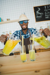 stylish african american bartender pouring lemonades into glasses on bar counter in cafe