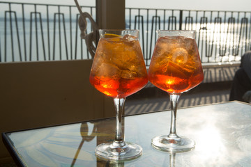 Waiter prepared the Aperol Sprits summer cocktail with Aperol, prosecco, ice cubes and orange in wine glass, ready to drink on sunny terrace
