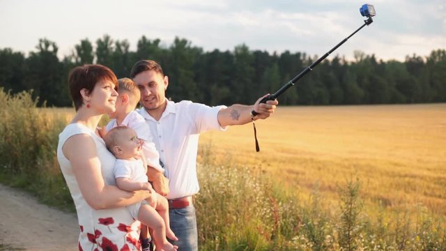 Happy family takes selfie at action camera in sunset. Family makes self portraits photos with cell phone in beautiful sunny landscape.