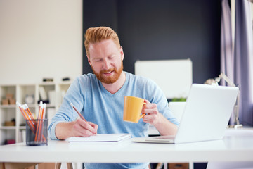 Businessman writing notes while sitting and drinking coffee in modern office