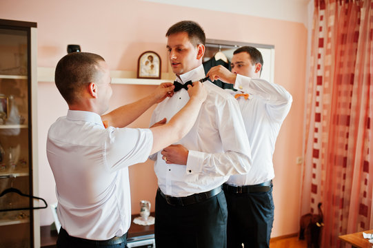Helpful groomsmen or bestmen helping groom to get ready for his wedding.