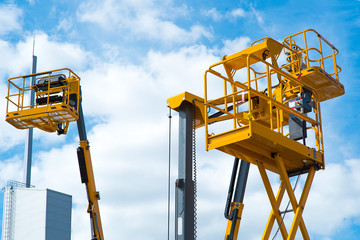 Hydraulic lift platform with bucket of yellow construction vehicle, heavy industry, blue sky and white clouds on background