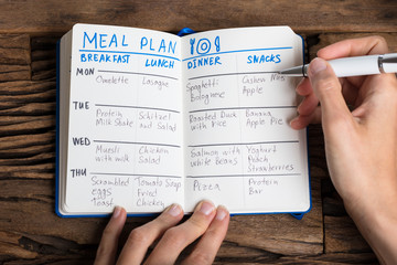 Person's Hand Filling Meal Plan On Notebook