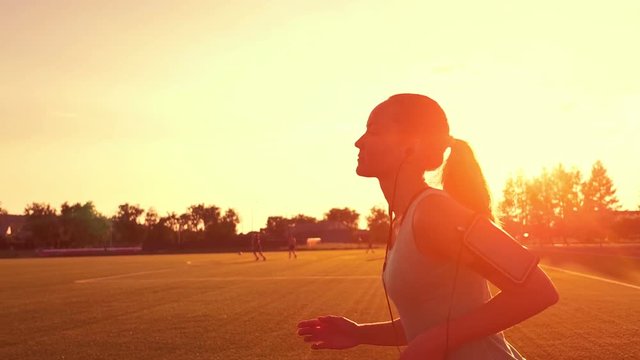 Runner running in a suburb, healthy fitness wellness vitality athlete silhouetted against the sun flare. Young woman running at the stadium at sunset