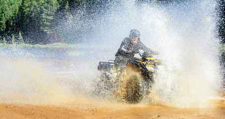 Man driving ATV quad through splashing water with high speed.