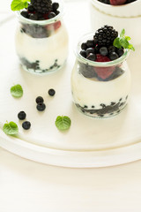 Healthy breakfast: yogurt with strawberry, blueberry and blackberry decorated mint leaves on white wooden table. Selective focus. Warm light