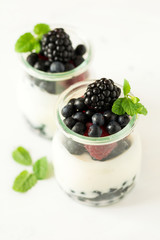 Healthy breakfast: yogurt with strawberry, blueberry and blackberry decorated mint leaves on white wooden table. Selective focus. Warm light