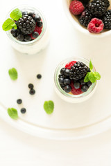 Healthy breakfast: yogurt with strawberry, blueberry and blackberry decorated mint leaves on white wooden table. Selective focus. Warm light
