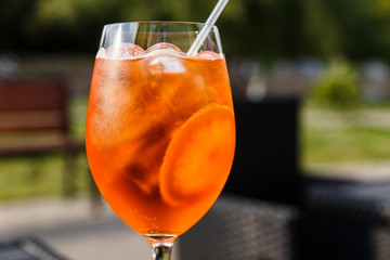 Aperol spritz in a wine glass with slices of orange and ice cubes inside. On a terrace of a city...