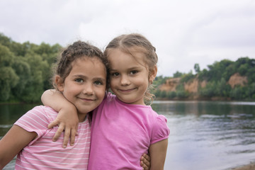 In the summer, two young friends stand embracing on the river bank.