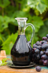 Black old balsamic vinegar in a glass jug with fresh red grapes on green vineyard background