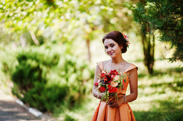 Attractive bridesmaid in orange dress posing with bridal bouquet on a wedding day.