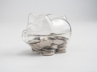 transparent see through piggy bank filled with coins on white background.