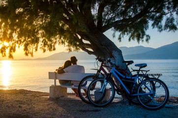 Fototapeta premium A couple of lovers watching the sunset sitting on a bench by the sea.