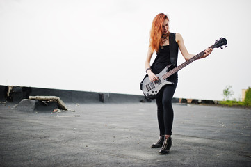 Red haired punk girl wear on black with bass guitar at the roof.