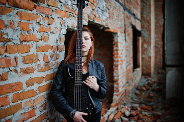 Red haired punk girl wear on black with bass guitar at abadoned place. Portrait of gothic woman...