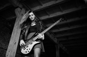 Red haired punk girl wear on black and red skirt, with bass guitar at abadoned place. Portrait of...