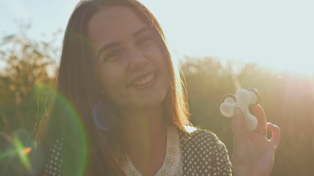 Young girl holding and rotates in the rays of the evening sun a white and black fidget spinners outdoors.