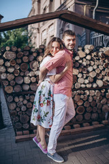 Fototapeta premium Stylish man and happy woman embrace in light on background of wooden firewood wall. Space for text. Happy couple are hagging, romantic moment.