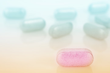 Obraz na płótnie Canvas Pink pill closeup on a background of other blue pills. On a light surface.