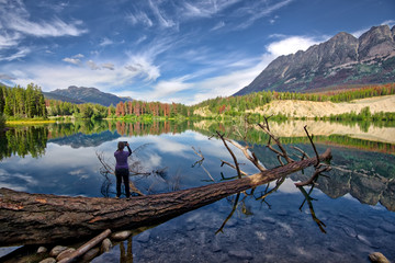 woman on floating log taking a picture of a lake