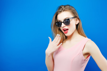 Portrait of Brunette Model Wearing Fashionable Sunglasses and Pink Dress on Blue Background. Perfect Girl is Posing in Studio.