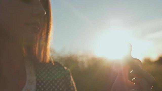 Young girl holding and rotates in the rays of the evening sun a white fidget spinners outdoors.