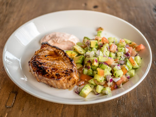 Healty LCHF meal. Pork stake with sallad including cucumber, tomato, avocado, onion. Plate on wood table.