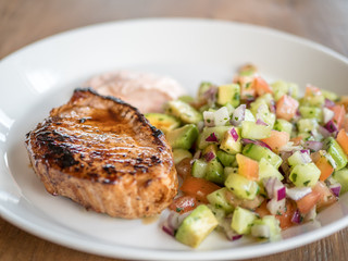 Healty LCHF meal. Pork stake with sallad including cucumber, tomato, avocado, onion. Plate on wood table.