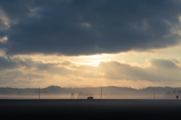 Single car driving through misty landscape with dramatic clouds and light