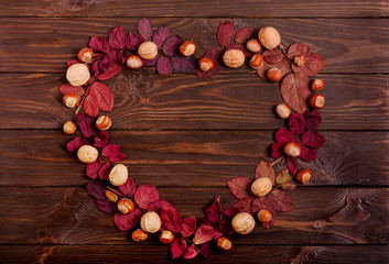 Flat lay frame in the form of a heart of autumn crimson leaves, hazelnuts and walnuts on a dark wooden background.