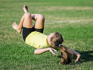 athletic little girl falling on grass after somersault. Loss of balance in air