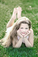 little beautiful girl with long loose hair on green grass at summer day