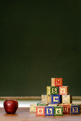 Apple and wooden blocks in front of blackboard