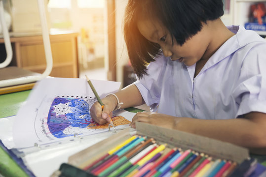 Asian Cute Little Kid Drawing,Adorable Little Girl Doing Homework,bored Or Tired Asian Kid Writing On Paper.Little Child Doing Homework,stress For Exam,colored Pencils On Wooden Desk.Homework Concept