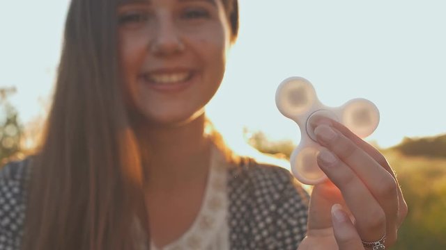 Young girl holding and rotates in the rays of the evening sun a white fidget spinners outdoors.