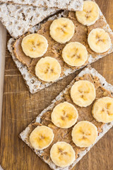 Healthy vegan homemade chunky peanut butter and banana sandwich with Swedish whole grain crispbread on wood cutting board, dessert, snack, diet, top view